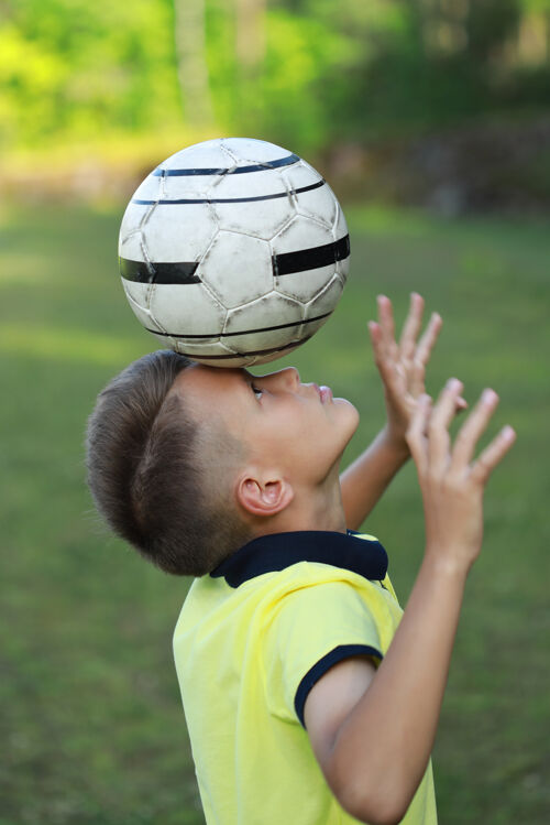 球员一个穿着黄色t恤衫的男孩站在足球场上 头上顶着一个球比赛游戏年轻