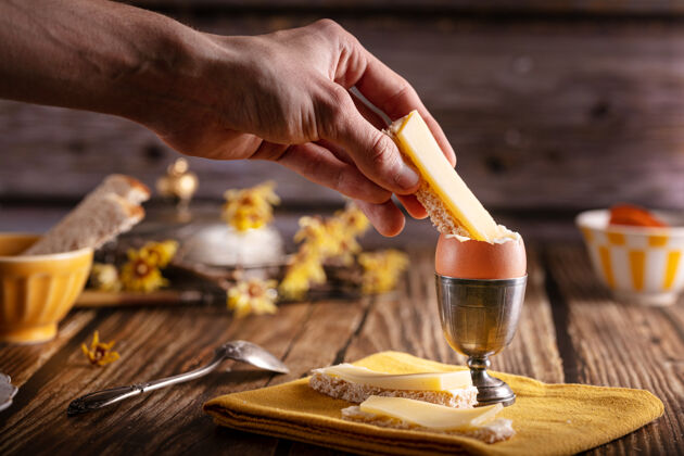 自制木桌上放着煮鸡蛋的银蛋杯 还有面包和奶酪传统美味奶酪