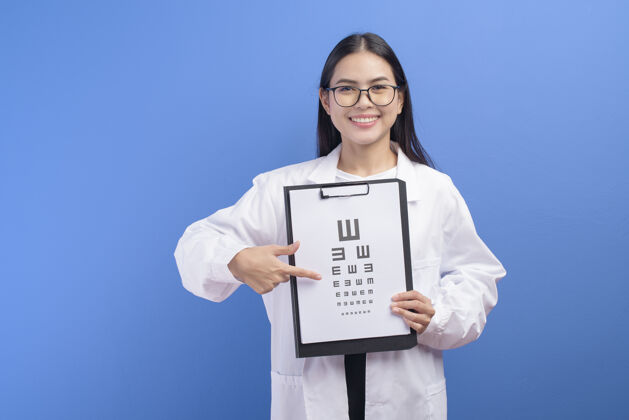 眼科一位年轻的女眼科医生 戴着眼镜 把视力表举在蓝色的墙上 健康的概念医学视力视力