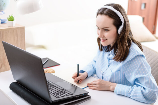 放松戴着耳机的白种女人在笔记本上写字 看着笔记本屏幕视频通信通信商务