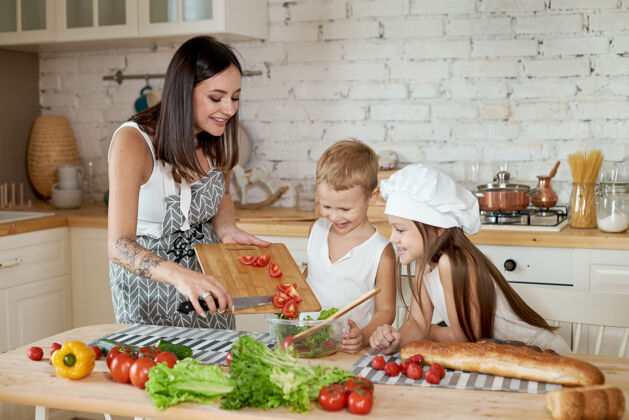 父母家人在厨房准备午餐妈妈教女儿和儿子准备一份新鲜蔬菜沙拉健康的天然食品 儿童维生素年轻妈妈饮食