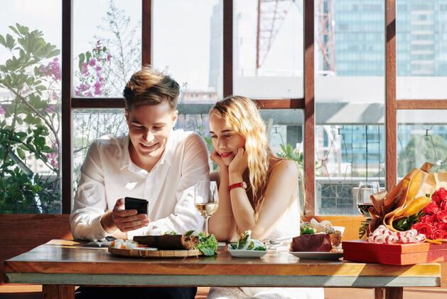 感情快乐的年轻女子在咖啡厅享受晚餐 在智能手机上看有趣的视频喝酒晚餐情人节