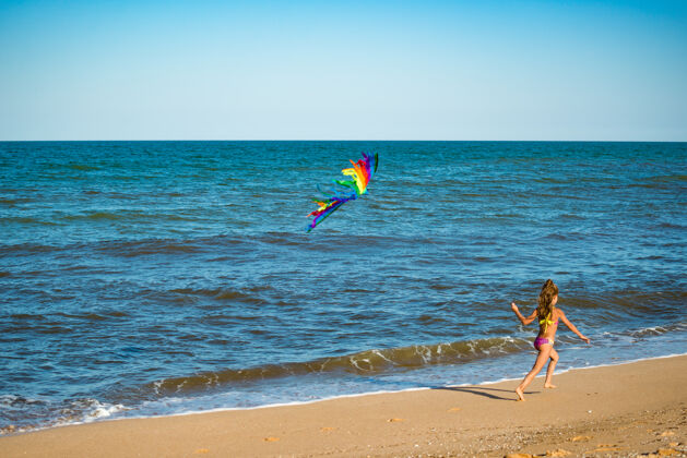 欢呼两个快乐的小女孩带着风筝在海边的沙滩上奔跑彩虹户外风筝