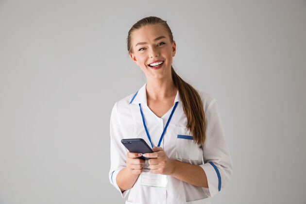 工人一位美丽快乐的年轻女美容师医生隔着灰墙 拿着手机在用外科职业手机