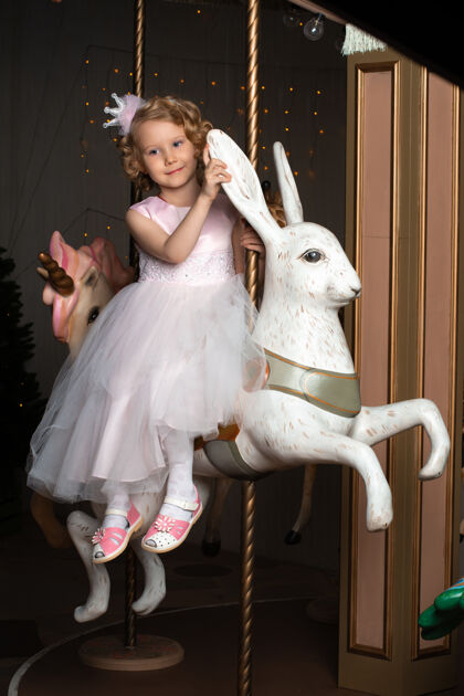 女儿一个穿着粉色裙子戴着皇冠的小女孩和一只白兔坐在旋转木马上家庭美丽小