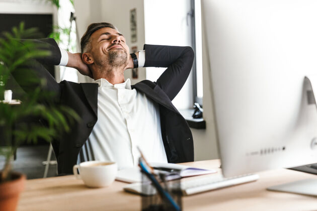 吸引力30多岁的快乐商人穿着西装 坐在办公桌前 在办公室里用电脑工作 微笑着的照片成人经理工作场所