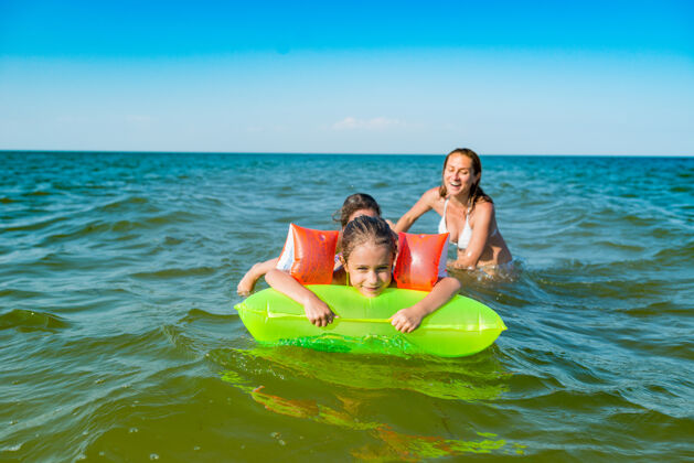海浪在一个阳光明媚的夏日 快乐的妈妈和两个积极的小女儿用气垫在海里洗澡游泳海边床垫水
