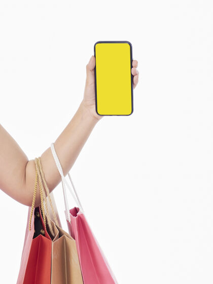 服务拿着白屏智能手机和白墙上购物袋的女人们营销路径消费者