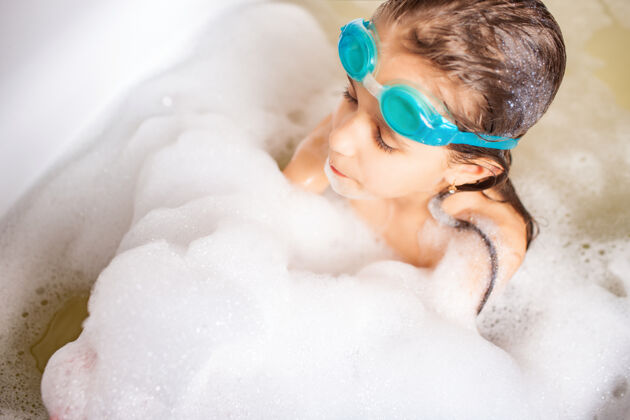 人类戴泳镜的漂亮蓝眼睛小女孩在泡沫浴缸里洗澡保健浴缸泡泡