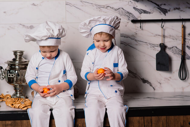 童年两个可爱的双胞胎男孩坐在地板上 快乐地吃着健康的食物 年轻的厨师水果小吃白色