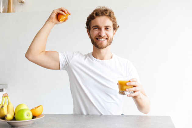 柔软图为一位快乐的留着胡子的年轻人在家里的餐桌上用水果做果汁 露出肱二头肌教育早餐吸引力