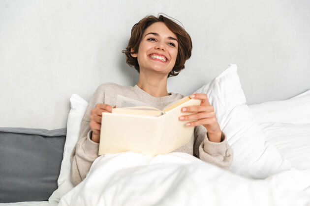 卧室微笑的年轻女孩 早上在床上放松 看书阅读休息女人