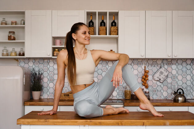 成人一位穿着运动服的女运动员在轻便的现代厨房的桌面上摆姿势美丽 健康 营养的概念身体水美丽