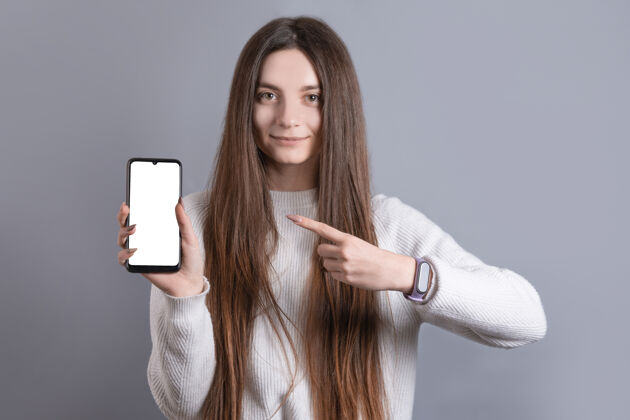手机一个年轻漂亮的女孩的肖像 一头乌黑的长发 轻松地微笑着 手指成人应用程序屏幕