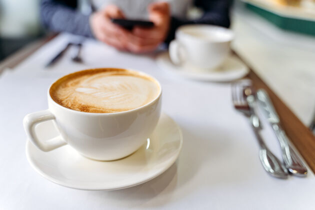 拿铁在咖啡店的桌子上放一杯咖啡打电话的人杯子休息饮料