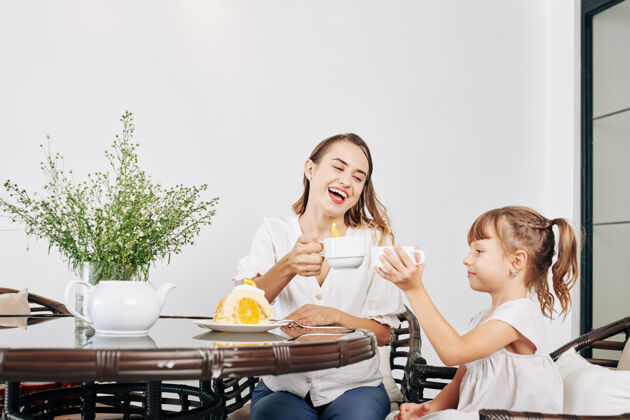 母亲快乐漂亮的年轻女子和小女儿一起喝茶吃自制饼干卷享受切片父母