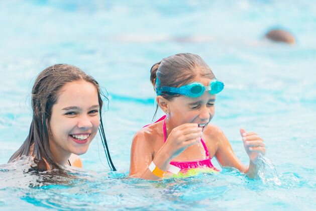 活跃在一个阳光明媚的夏日 两个可爱的小姐妹在游泳池里游泳孩子妹妹年轻