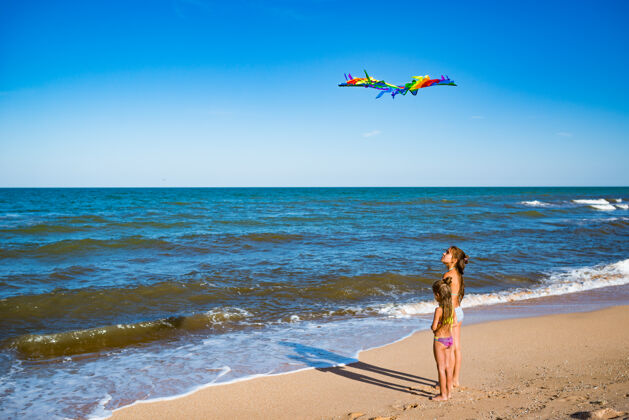 姐妹在一个阳光明媚的温暖夏日 两个快乐的小女孩姐妹在海边的沙滩上玩风筝明亮风温暖