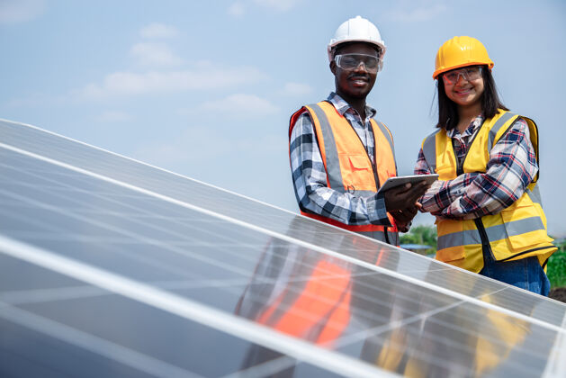 再生两名工人和技术人员在玉米地的高钢平台上安装重型太阳能光伏板清洁能源的光伏组件理念绿色环保清洁技术人员电力