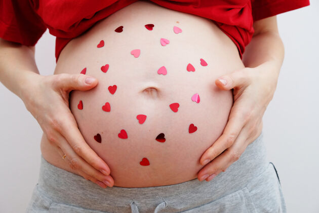 肥料情人节快乐肚子上有心形亮片的孕妇母亲的概念婴儿淋浴拥抱女性爱抚