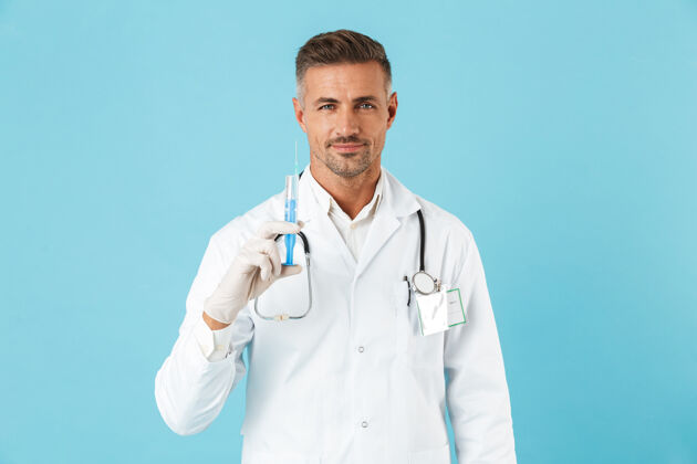 救护车英俊的医生戴着听诊器戴着手套拿着注射器 孤立地站在蓝色的墙上医院医生心脏病专家