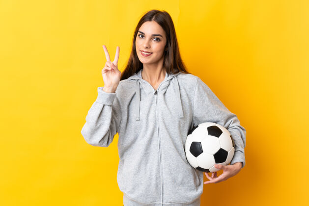 手势年轻的足球运动员黄色的女子微笑着 并显示胜利的标志球足球竞争