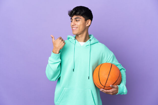 手指年轻人打篮球越过孤立的紫色墙壁指向一边 提出一个产品运动员看微笑