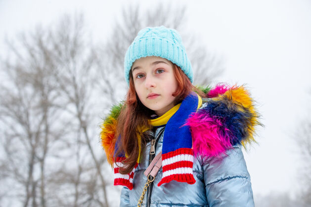 少年冬日少女的画像在她的温暖服装女孩在下雪的天气里戴一顶蓝帽子漂亮模特美丽