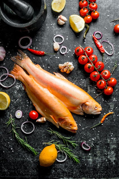 动物生鱼鳟鱼配辣椒 樱桃番茄和柠檬放在深色的乡村餐桌上厨房特色辣椒