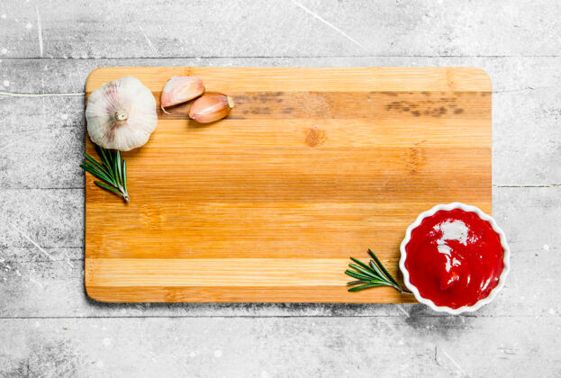 香草木桌上放着番茄酱 大蒜和迷迭香树枝的空木板空烹饪大蒜