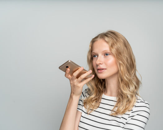 白站在白色墙壁附近 灰色背景 漂亮的女性在手机上口述语音信息电话手机金发