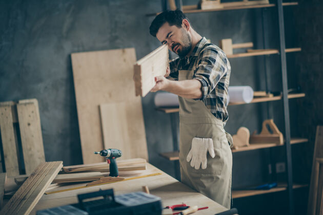 工匠他的肖像他漂亮迷人专注熟练勤劳的家伙看着测量光滑的木板在家里现代工业阁楼砖风格室内木材修理木匠
