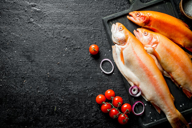 鳟鱼新鲜的生鳟鱼和西红柿放在黑色的乡村餐桌上切割配料番茄