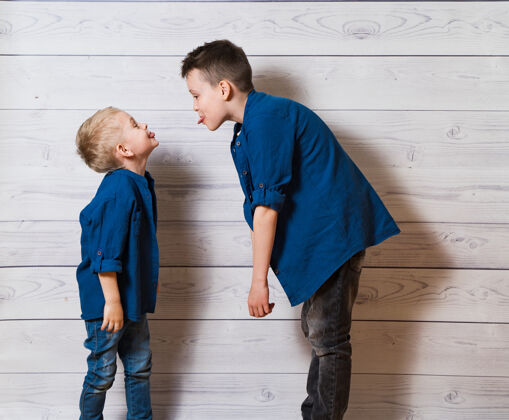 站立两个穿着便服的男孩 穿着白色的木头衣服 互相吐舌头孩子室内可爱