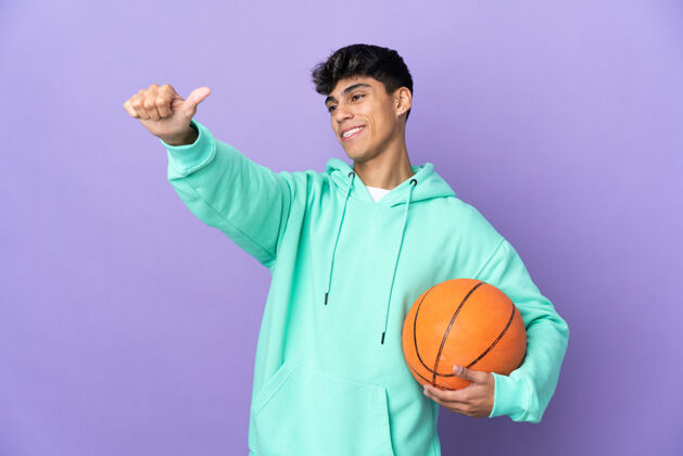 运动年轻人在孤立的紫色墙壁上打篮球 竖起大拇指好运动员成功