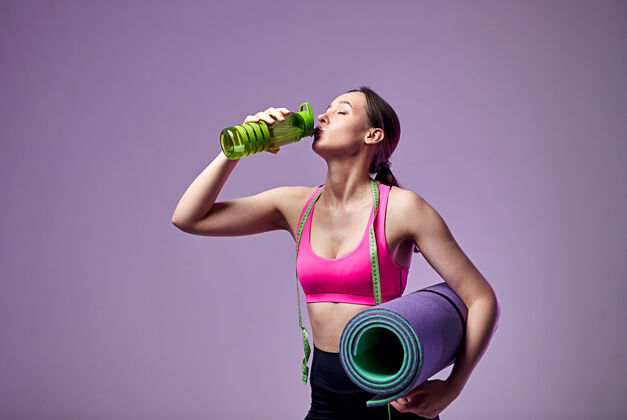 教练穿着运动服的运动美女 手里拿着一瓶水和一张紫色的健身垫去健身房吧健身房健身运动