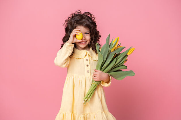 复活节彩蛋有趣的小女孩拿着郁金香和五颜六色的复活节彩蛋在她眼前的粉红色背景郁金香节日孩子