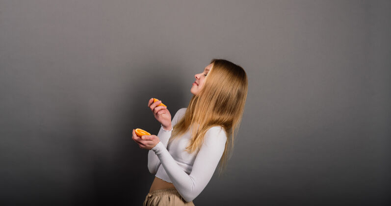 健康微笑的女人在工作室里吃橘子 半个水果 金色的长发持有成人肖像
