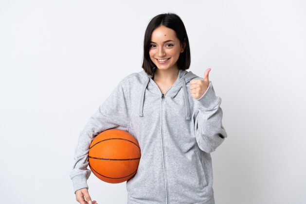 Ok年轻的白人女子孤零零地站在白墙上打篮球 竖起大拇指微笑比赛女人