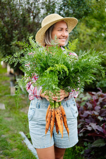 零戴着帽子的可爱女孩在花园里摘胡萝卜花园.秋天蔬菜丰收卷心菜生物生物