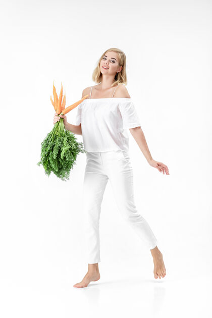 欢呼一个穿着白衬衫的金发美女 手里拿着一根新鲜的胡萝卜 上面有绿叶背景.健康还有节食维生素可爱膳食