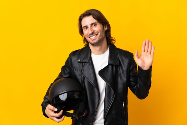 驾驶一个戴着摩托车头盔的人孤立地站在黄色的墙上 带着幸福的表情用手敬礼谚语看自行车