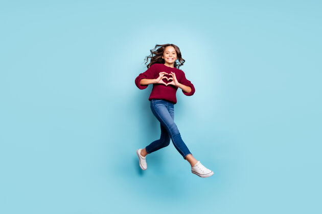 浪漫开朗正面女友跳楼跑步展示心形标志穿牛仔裤牛仔紫红色毛衣孤立蓝色生动色彩背景的全身照片休闲空气表演