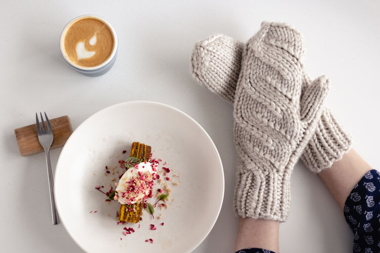 舒适女性手戴白色手套 拿着蛋糕和咖啡放在白色桌子上蛋糕.概念冬天 温暖 节日 事件时尚早晨甜点