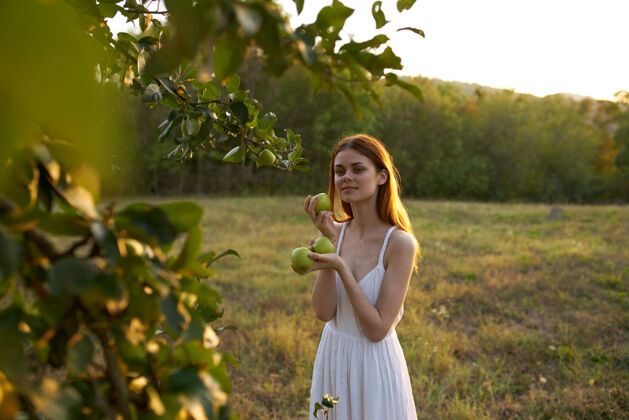 新鲜一个女人拿着熟透的苹果站在山上的草地上 背景是高大的树木成人美丽手