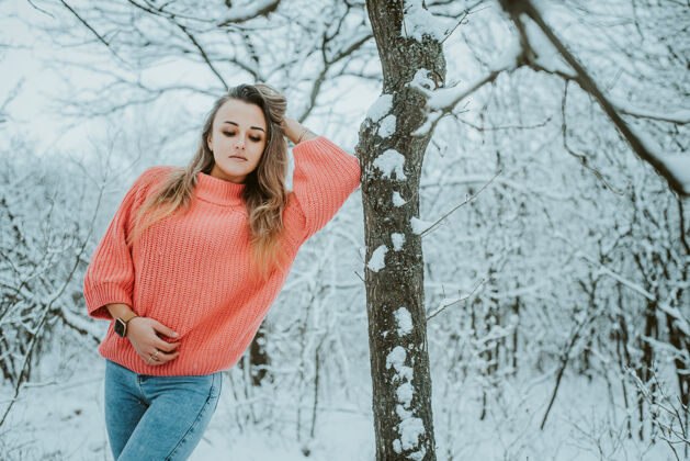 公园一个穿着粉色宽松毛衣和牛仔裤的漂亮女孩在寒冷的雪域森林里享受森林快乐