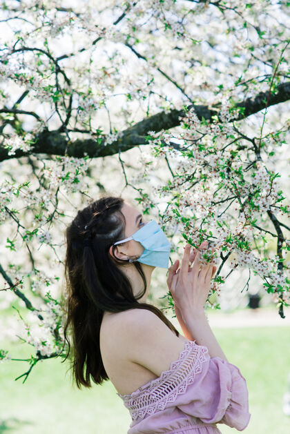 脸一个戴着防毒面具的女孩在春天的花丛中绽放花园.春天过敏和covid概念保护医学季节
