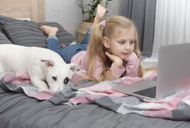 教训金发女孩在家上网学习笔记本电脑.儿童还有一只狗在床上青少年动物电子