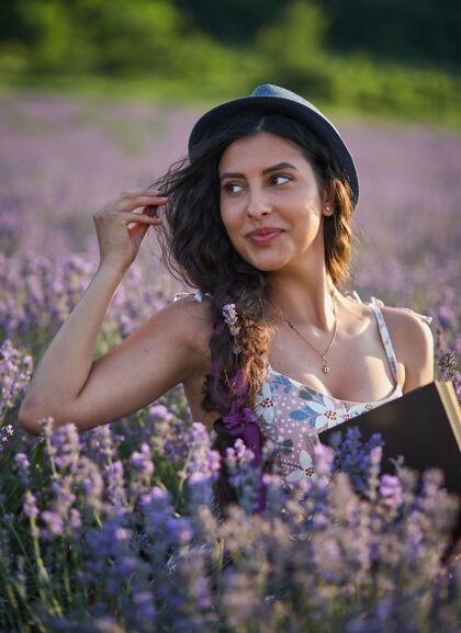 快乐戴着帽子的美女坐在紫色的薰衣草地里 手里拿着一本书田野放松自然