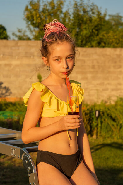 年轻在游泳池里喝果汁的孩子夏季酒吧与家人一起度假孩子小拿着新鲜菠萝鸡尾酒的女孩假期饮料柠檬水